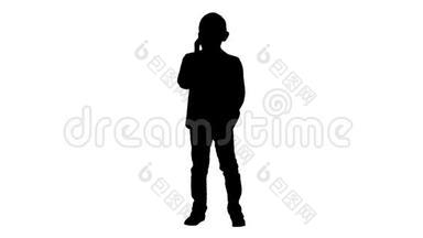 剪影可爱的小男孩在他的智能手机上说话，站在一套深色西装。